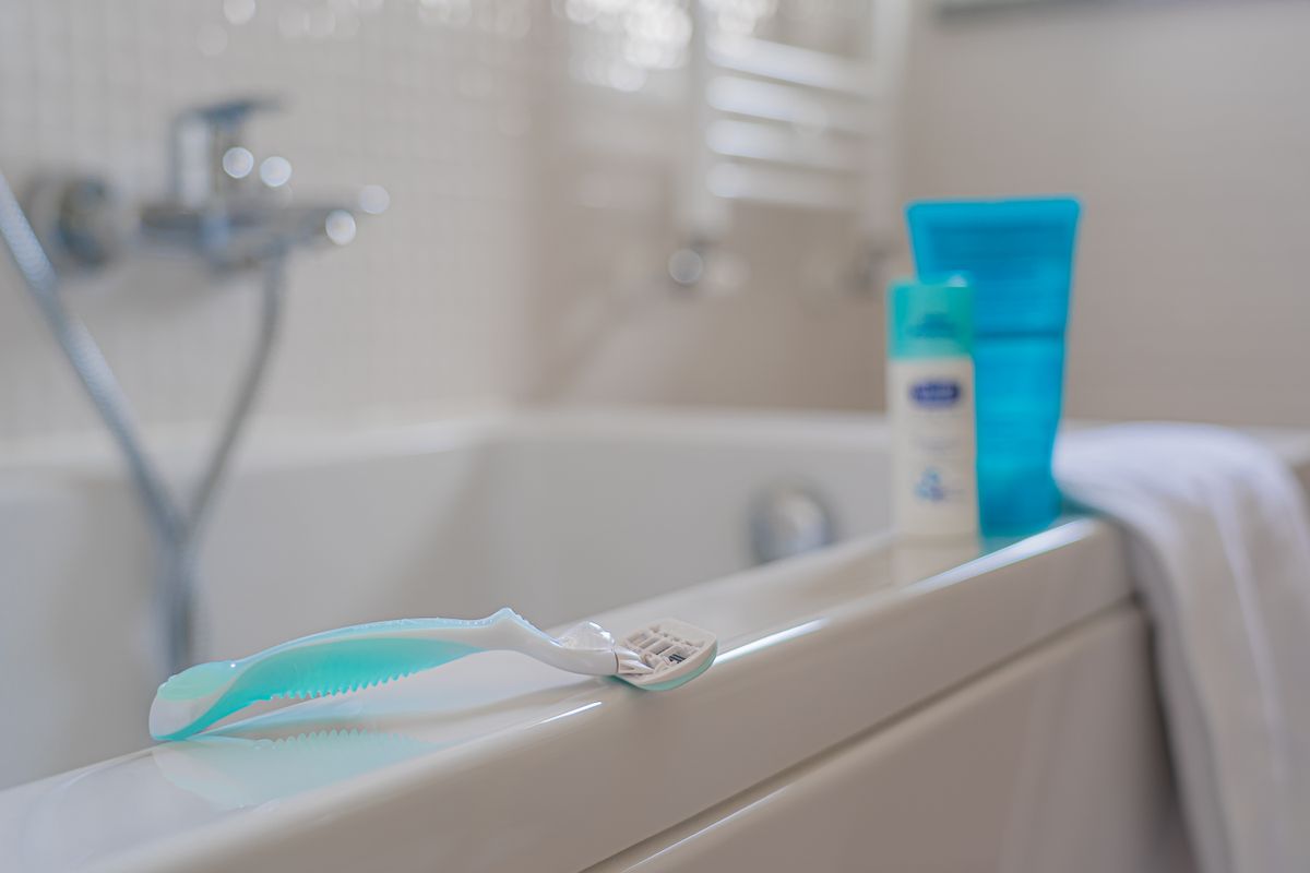 Close-up of a disposable razor on a bathtub edge with toiletries in a modern bathroom setting.