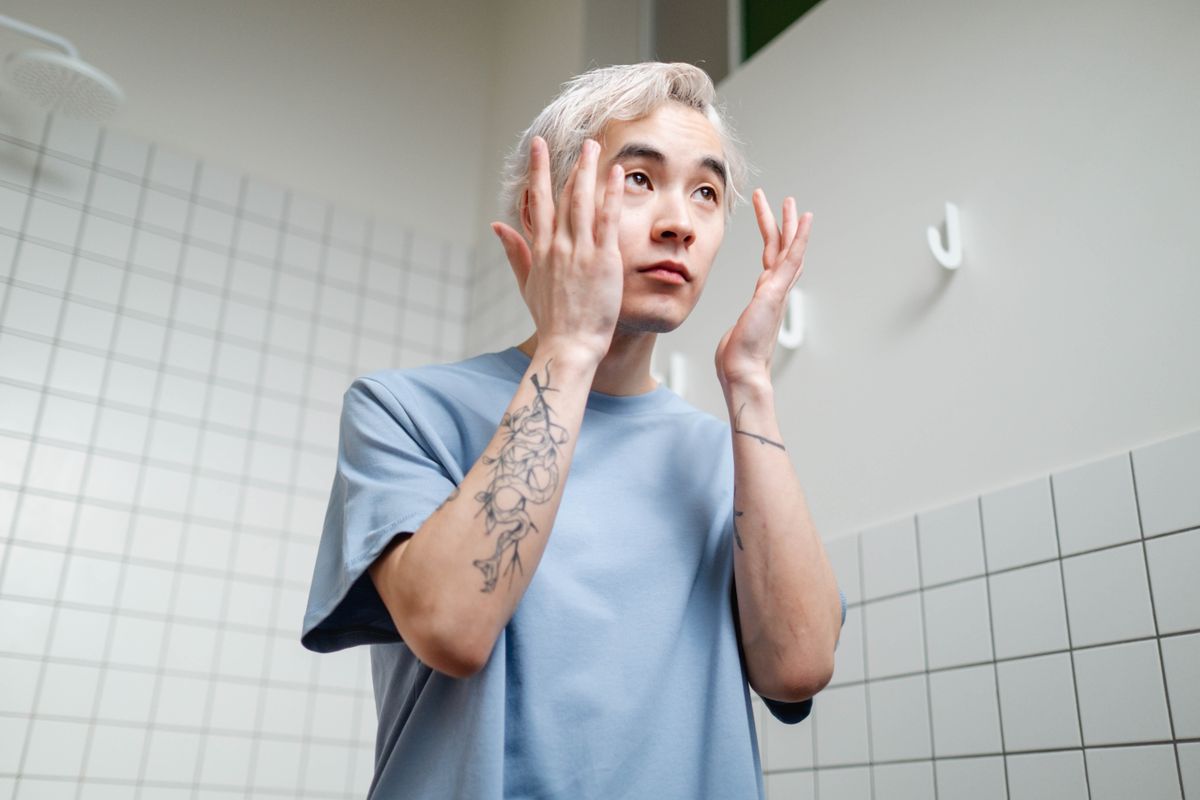 Young man applying skincare product in a contemporary bathroom setting.