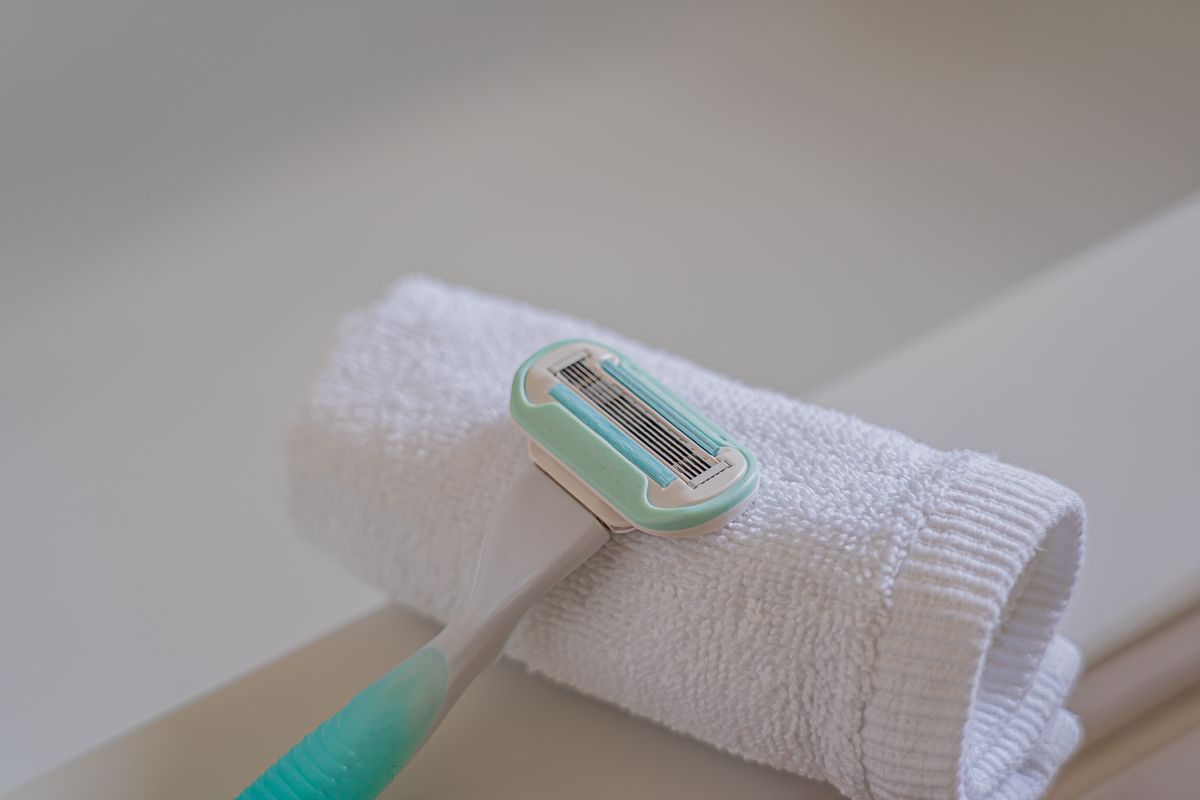 A disposable razor placed on a rolled white towel in a bathroom, highlighting grooming essentials.