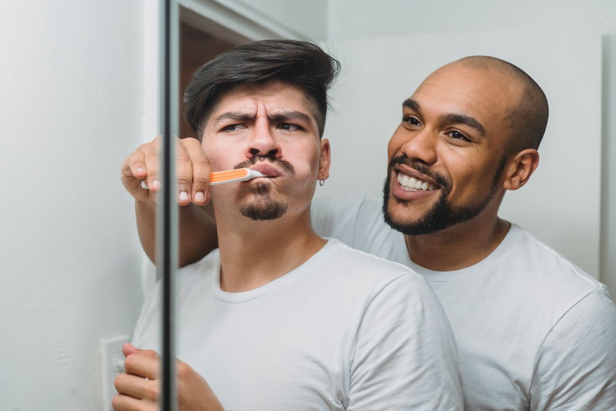 A happy interracial couple sharing a moment together, brushing teeth in front of the bathroom mirror.