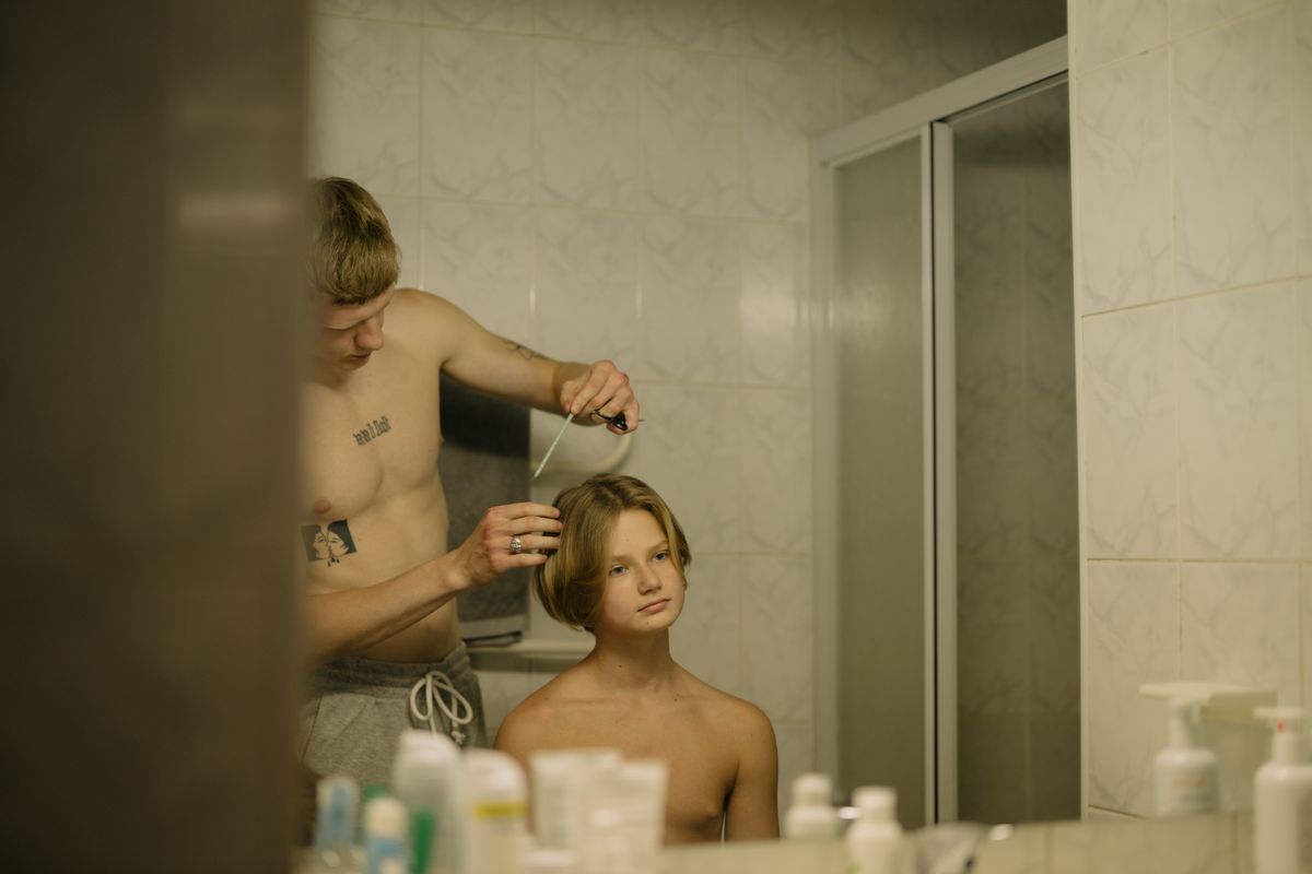 A young tattooed man combs his hair by a bathroom mirror, focusing on grooming.
