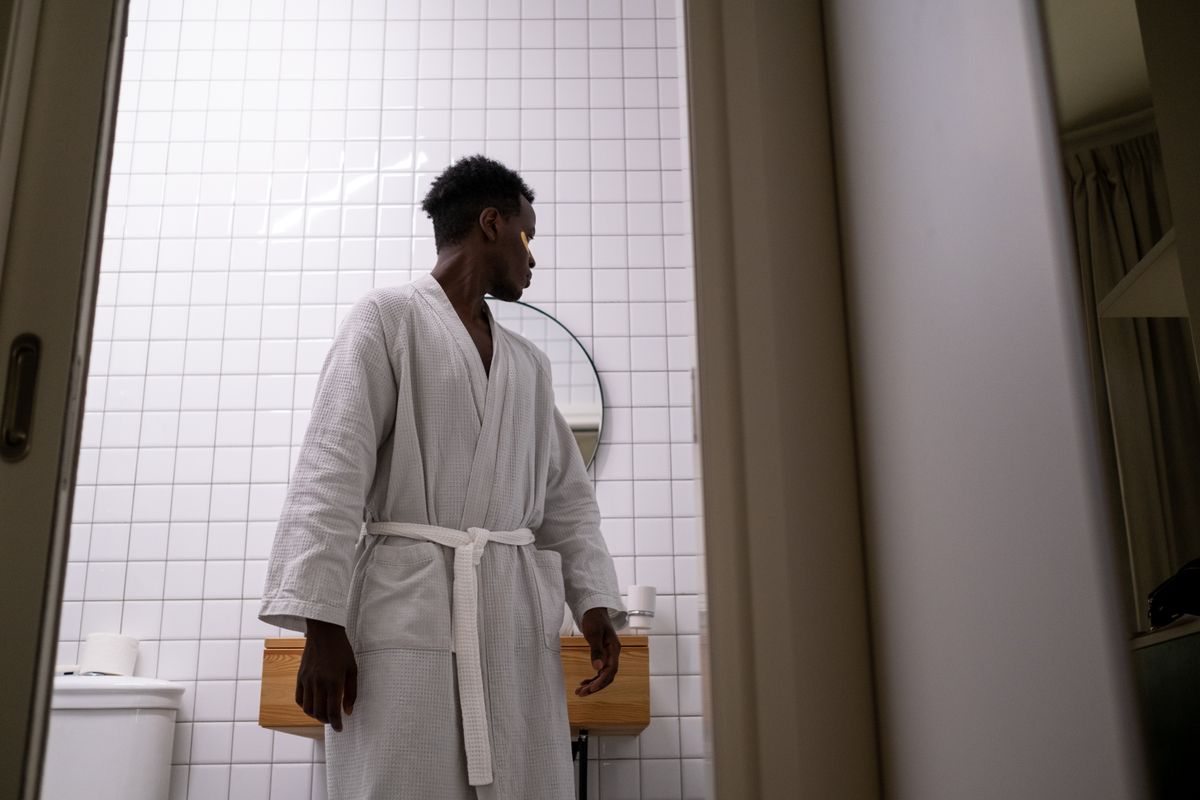 A man in a white bathrobe is looking behind him in a modern restroom with a mirror.