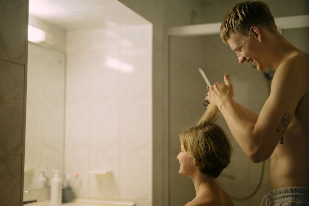 A man cuts a boy's hair in the bathroom, reflecting brotherly bonding and shared moments.