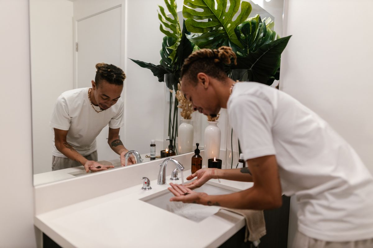 A young man washing his hands as part of his morning skincare routine in a modern bathroom.