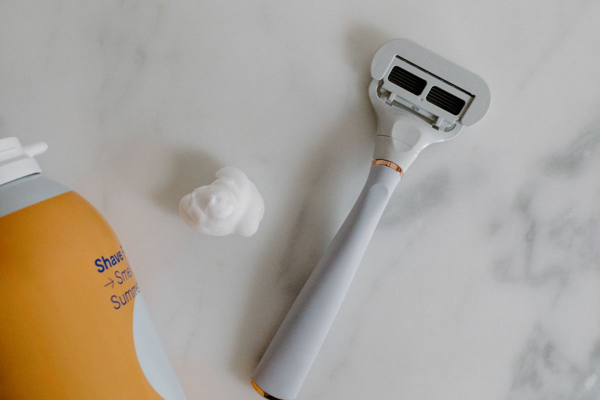 Top view of a razor and shaving foam on a marble surface, perfect for grooming and lifestyle themes.