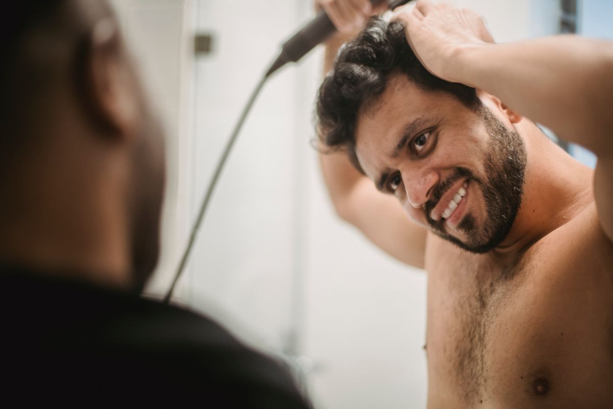 Smiling man styling hair in front of bathroom mirror, showcasing personal grooming and confidence.