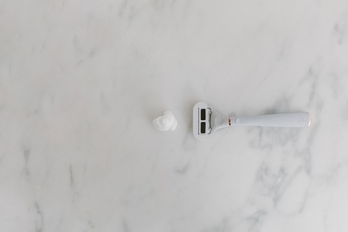 A minimalist scene with a shaving razor and foam on a marble background, offering copyspace.