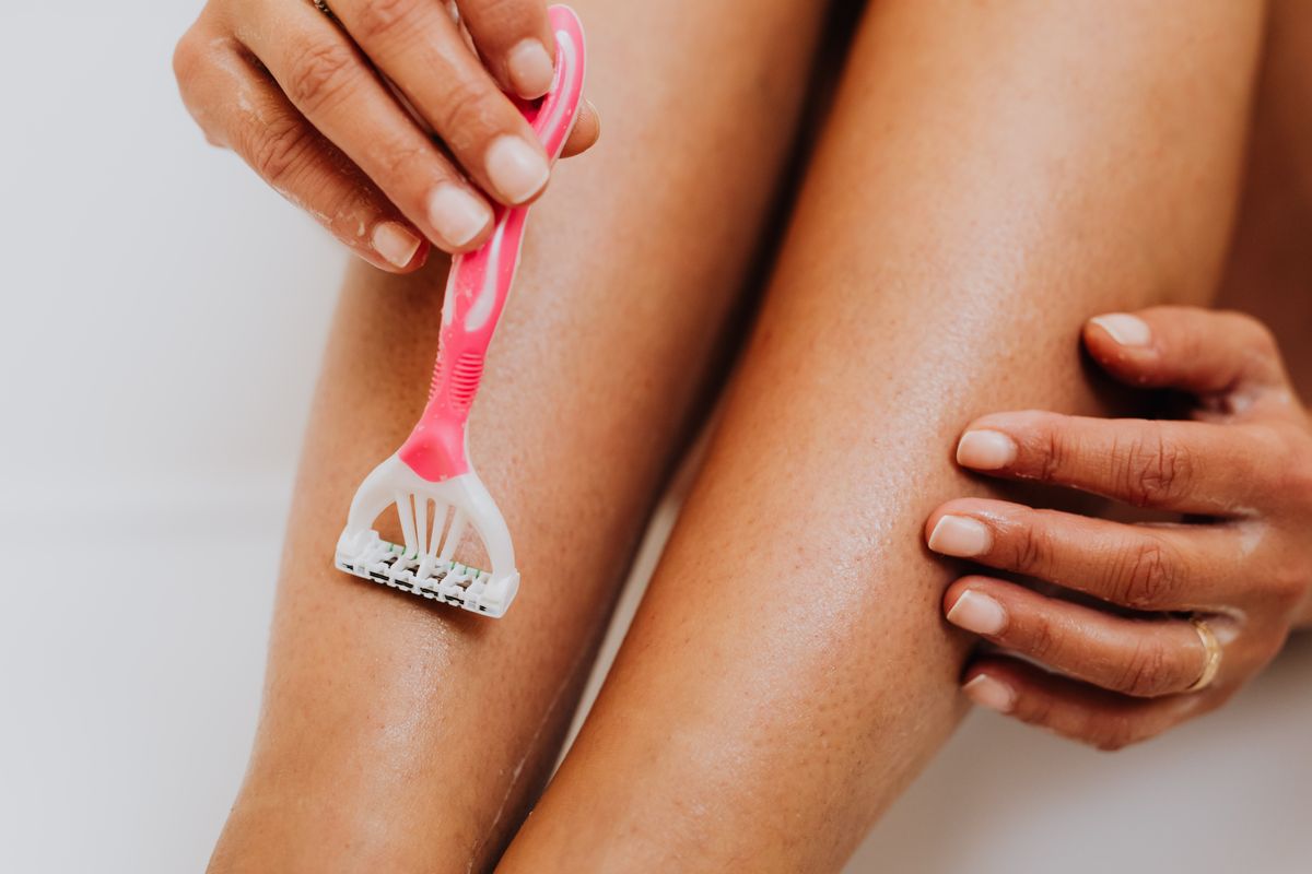 A close-up image of a person shaving their leg with a pink razor, focusing on smooth skin and personal care.