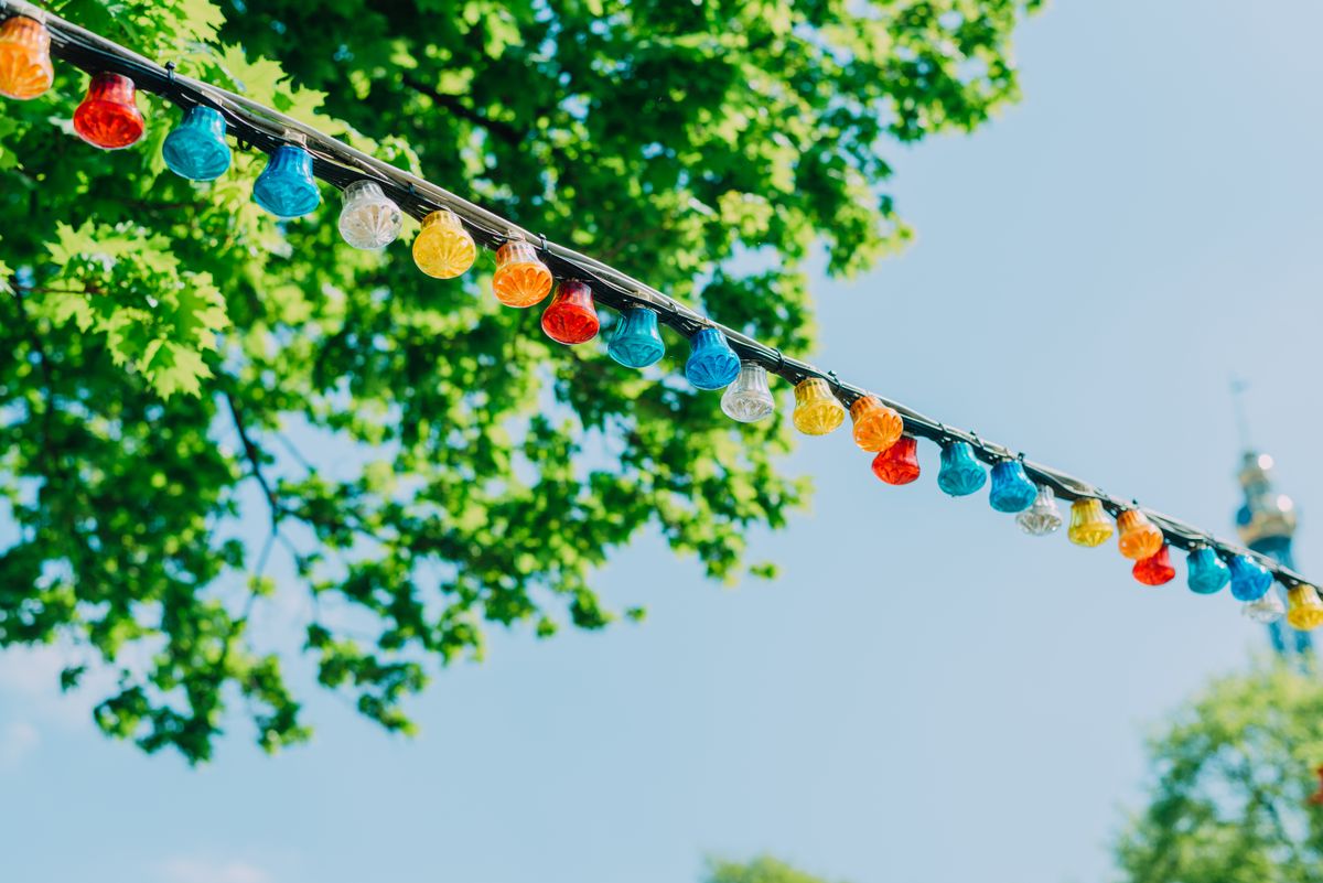 Brightly colored string lights in an outdoor Vienna park, surrounded by lush green trees and blue sky.