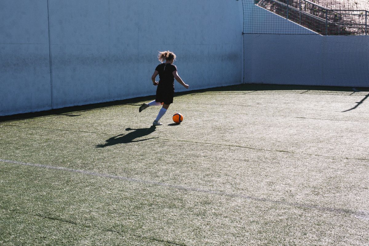 A young woman playing soccer, dribbling a ball on an outdoor field in daylight.