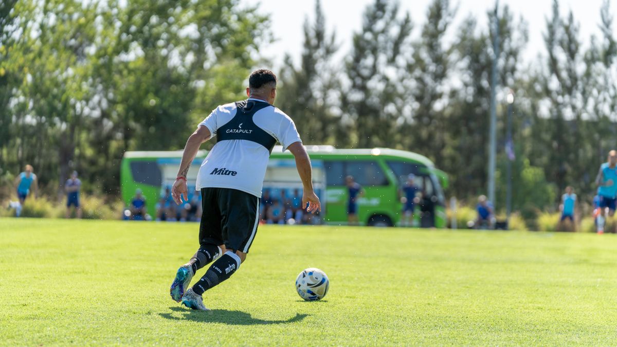 Soccer player in training, dribbling the ball on a sunny day with a green bus in the background.