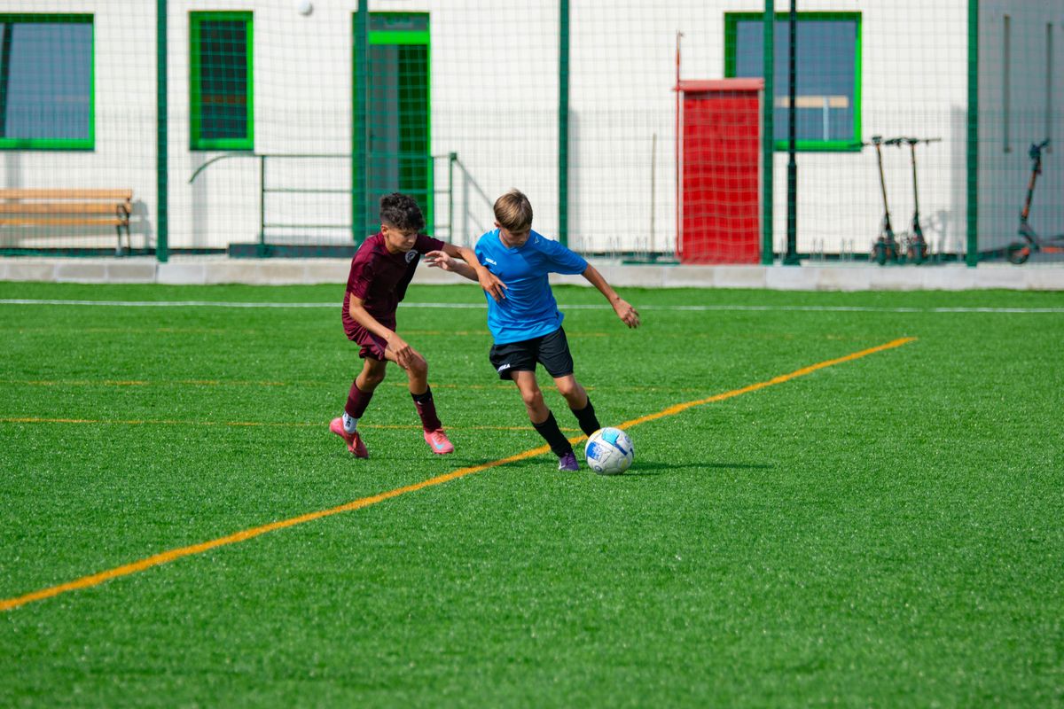 Two young boys playing soccer on an outdoor field in sunny weather.