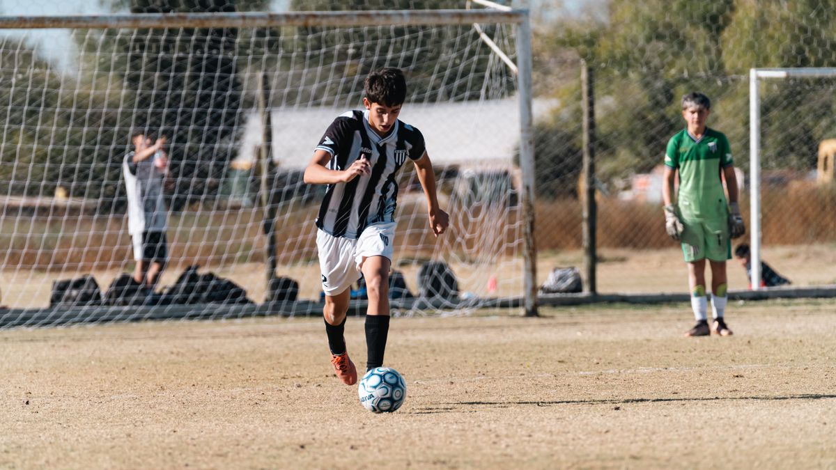 Teen soccer player dribbling the ball during a match on a sunny day outdoors.