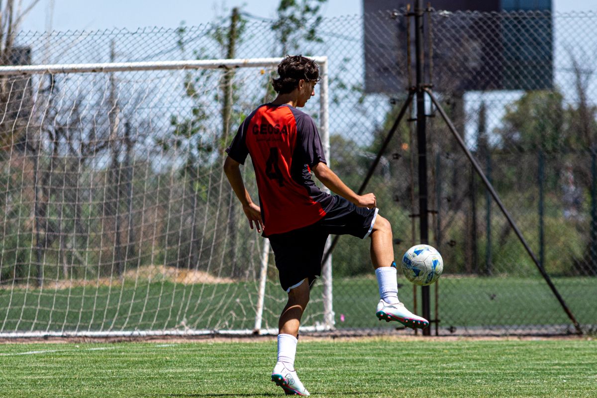 Teenager in red jersey playing soccer on an outdoor field during daytime.