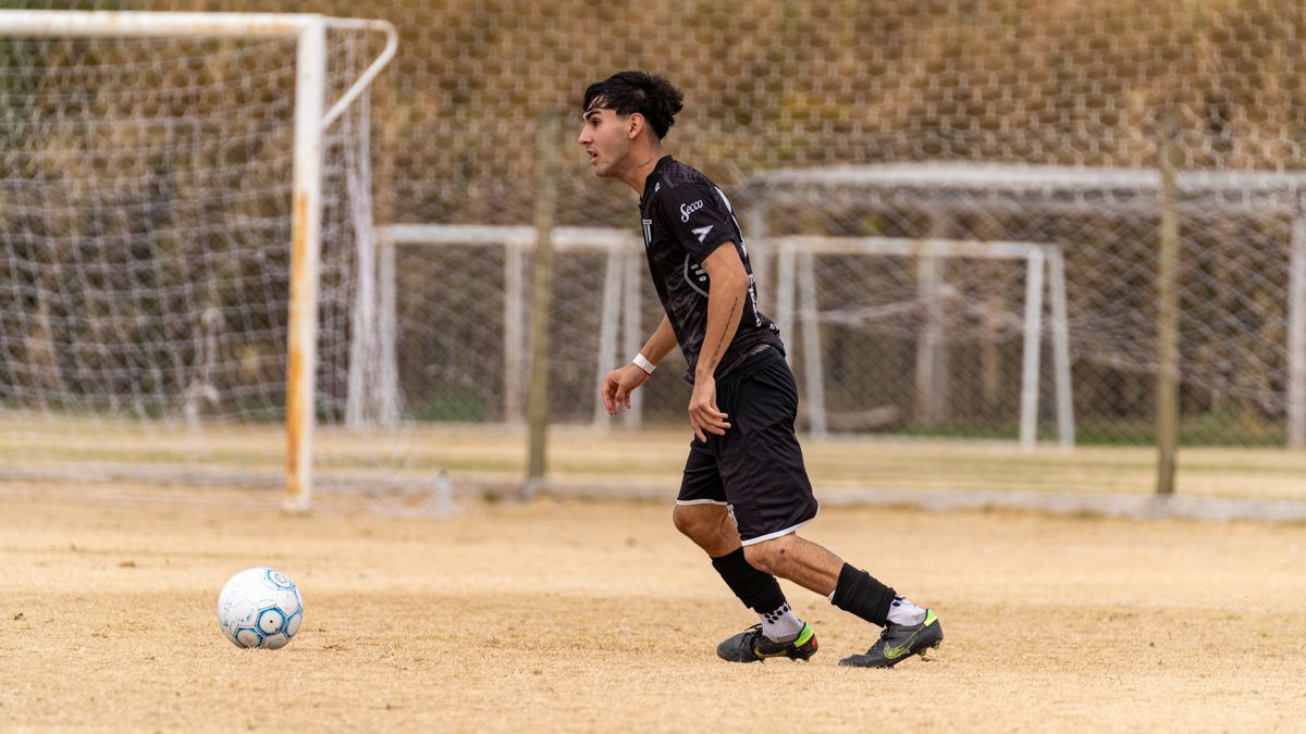 Young male soccer player in action on a grass field, focused on the ball during a game.