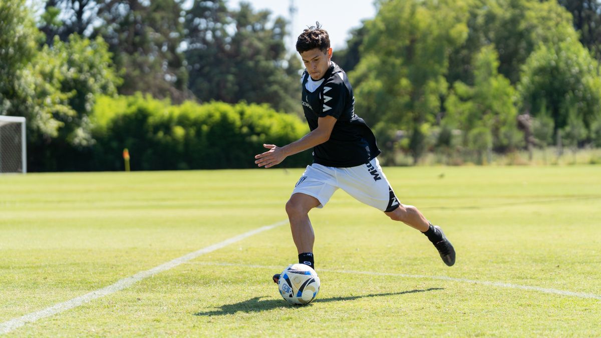 A teenager playing soccer on a sunny day, dribbling the ball on a grassy field.
