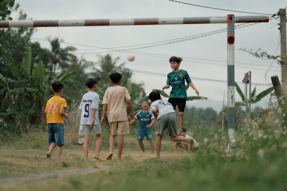 Boys enjoying a soccer game in a rural setting, surrounded by nature.