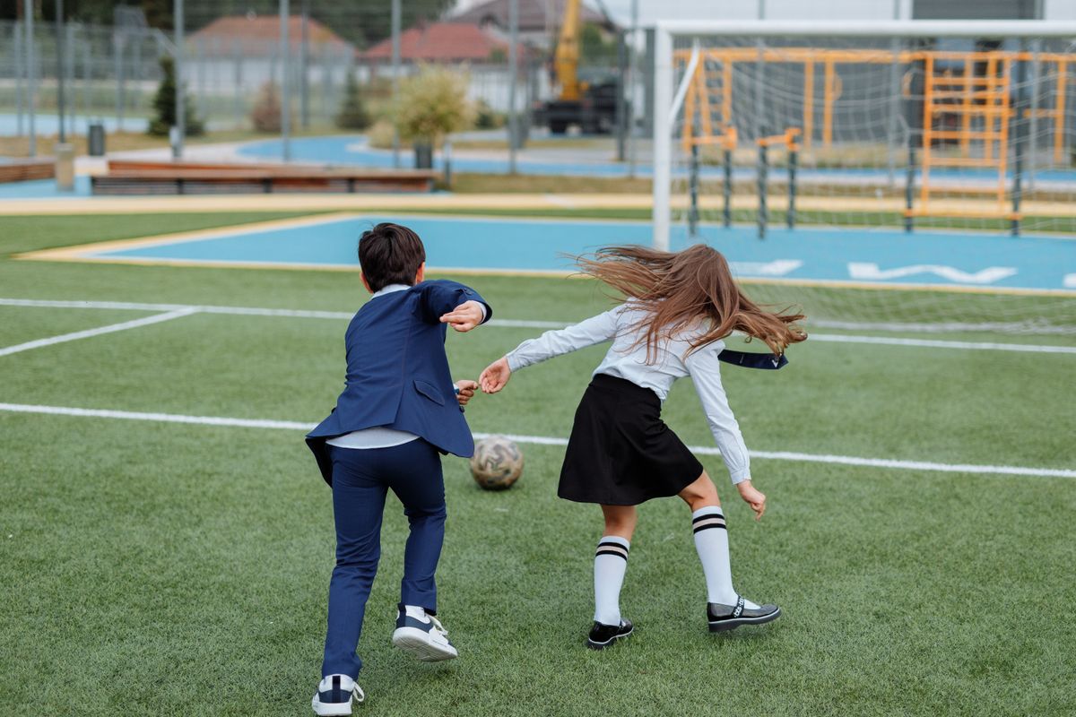 Two children in school uniforms playing soccer on a field, enjoying outdoor fun.