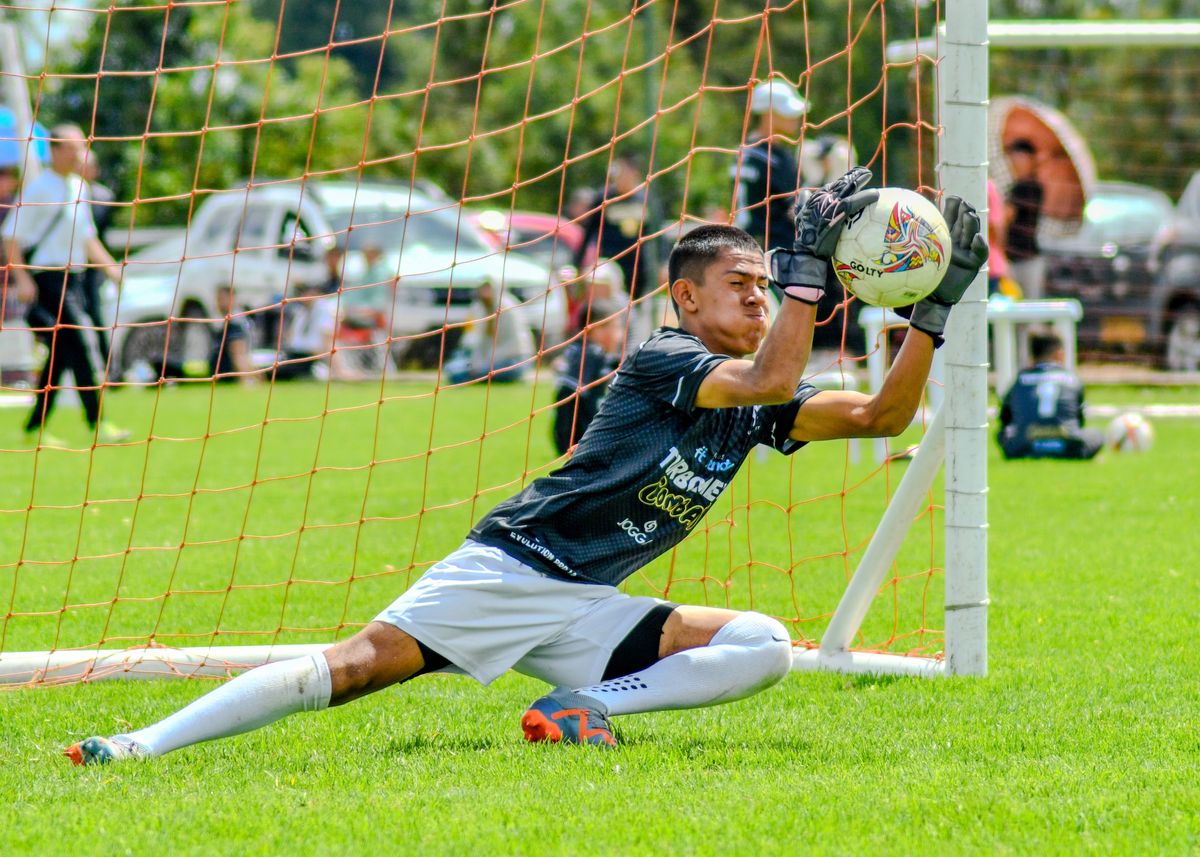 Dynamic action shot of a young goalkeeper catching a soccer ball during a match outdoors.
