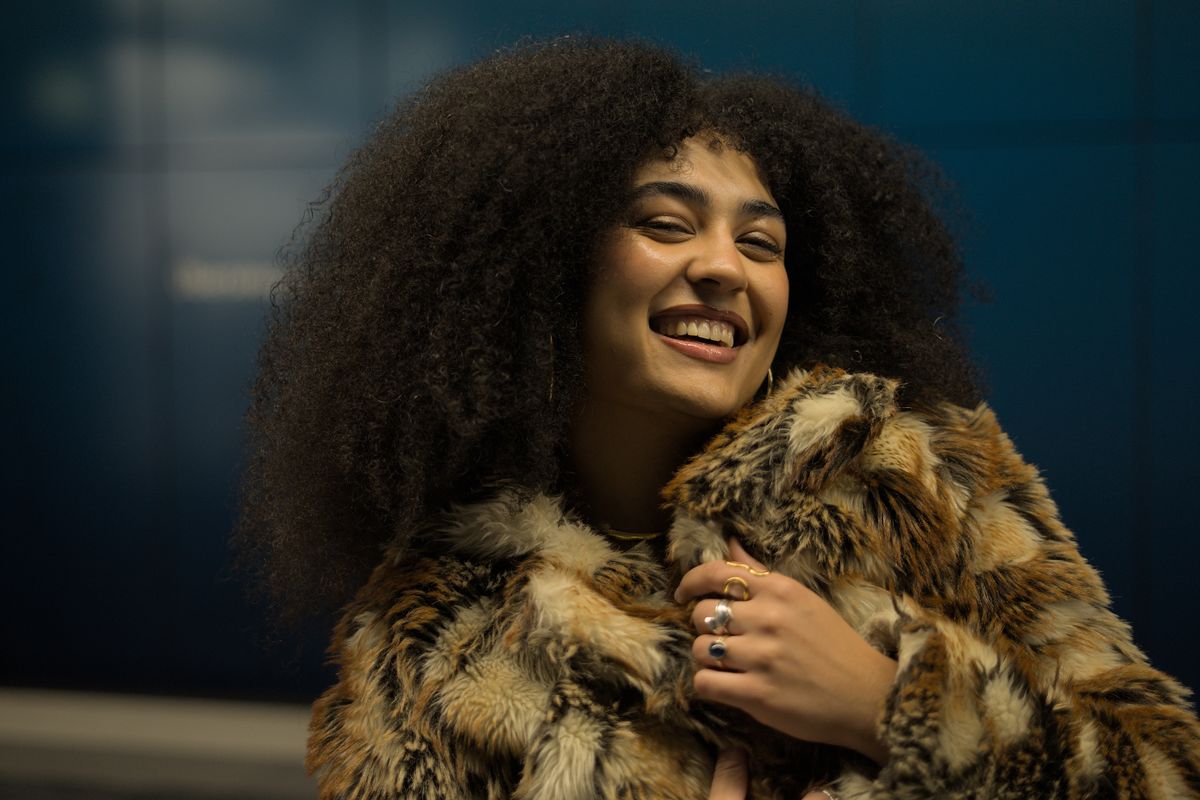 Joyful woman with curly hair in a stylish faux fur coat against a blue background.