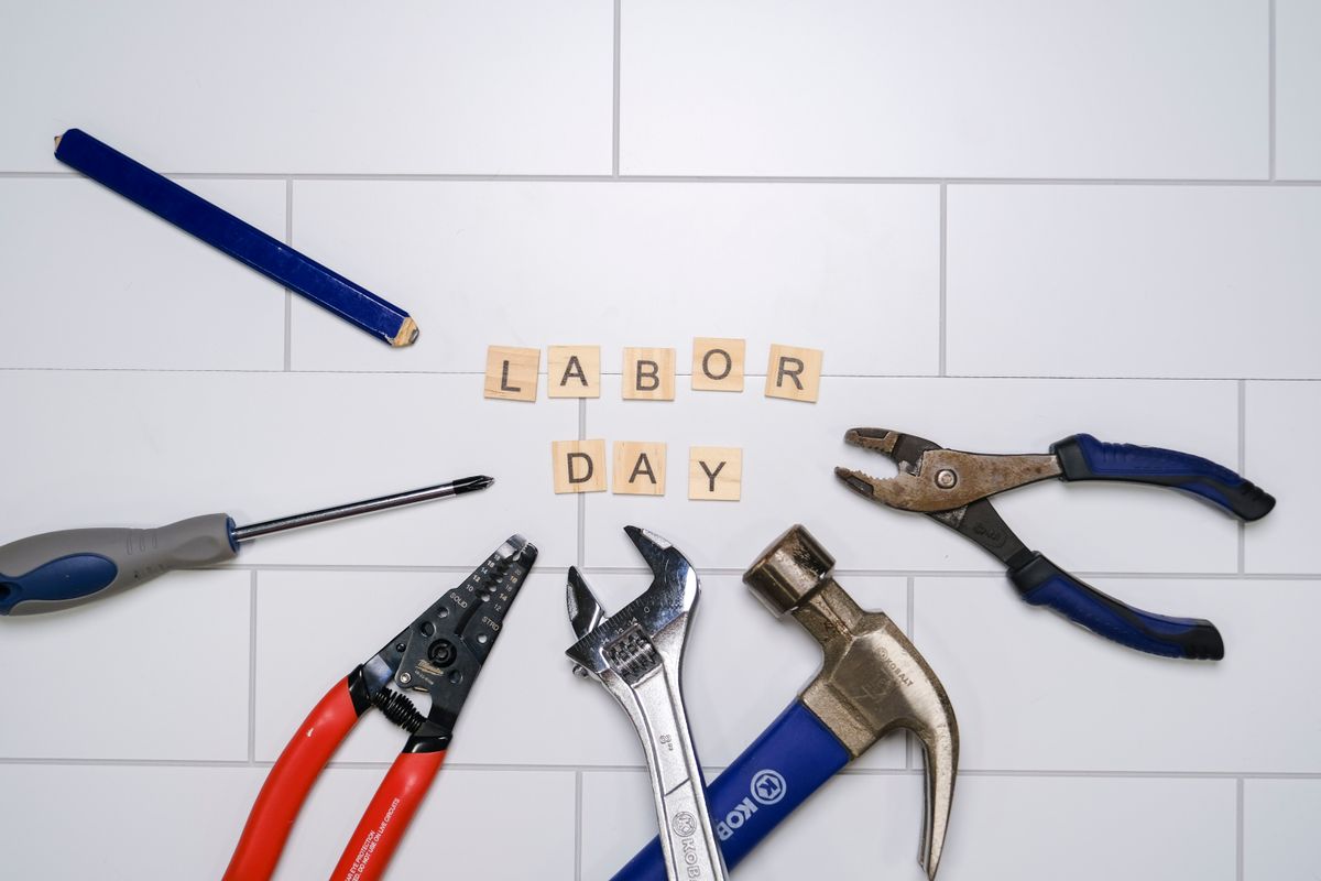 Flat lay of various hand tools around 'Labor Day' tiles on a white surface, symbolizing work and craftsmanship.