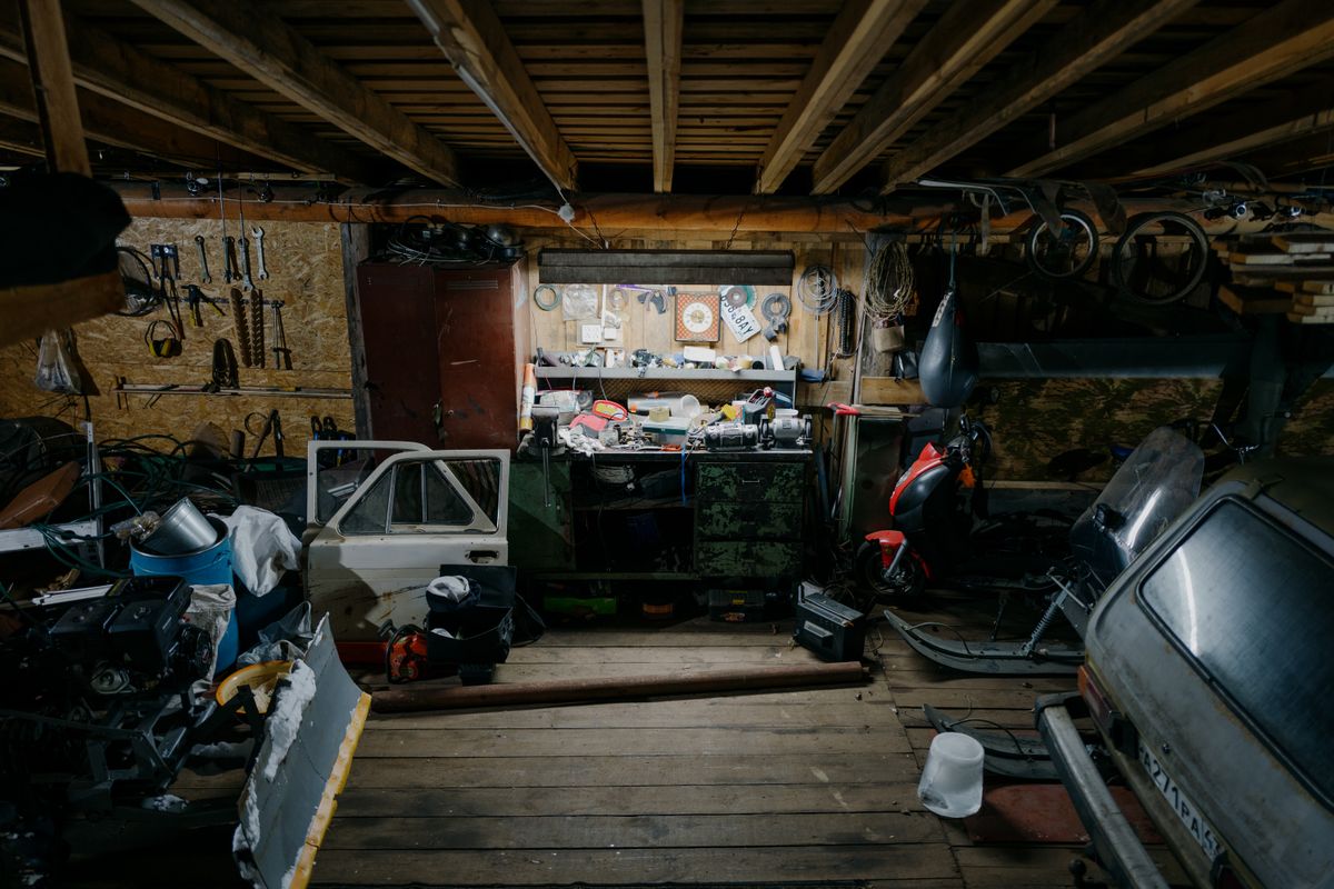A cluttered garage workshop filled with vintage tools, car parts, and motorcycles, showcasing a rustic work environment.