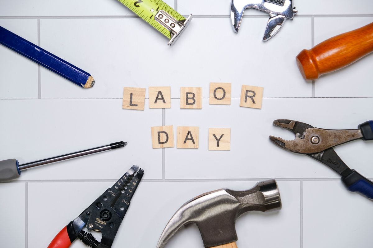 Top view of various tools with Labor Day text on white tiles, signifying the holiday and work.