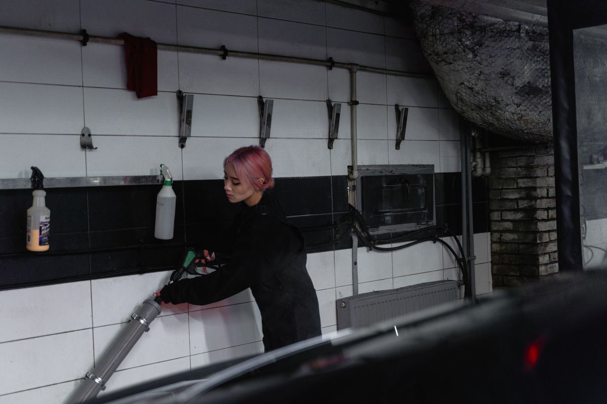 A young woman in a garage power sprays a vehicle, showcasing modern car maintenance.