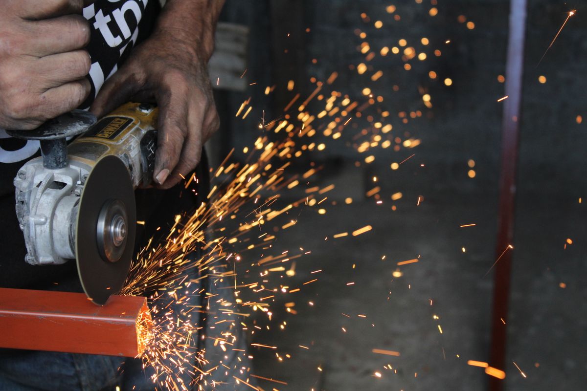 A worker using a power tool creates sparks while cutting metal, showcasing industrial craftsmanship.