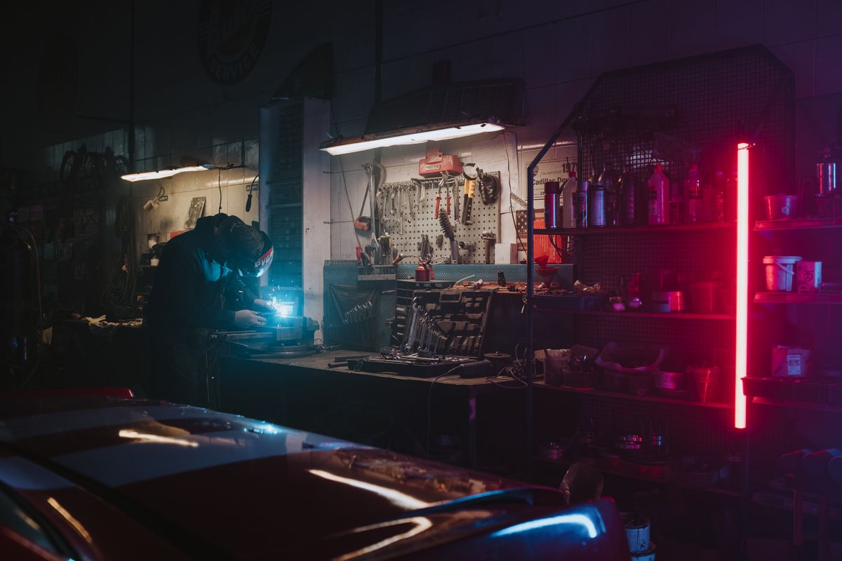 Mechanic working in a dimly lit garage, highlighted by neon lights and tools around.