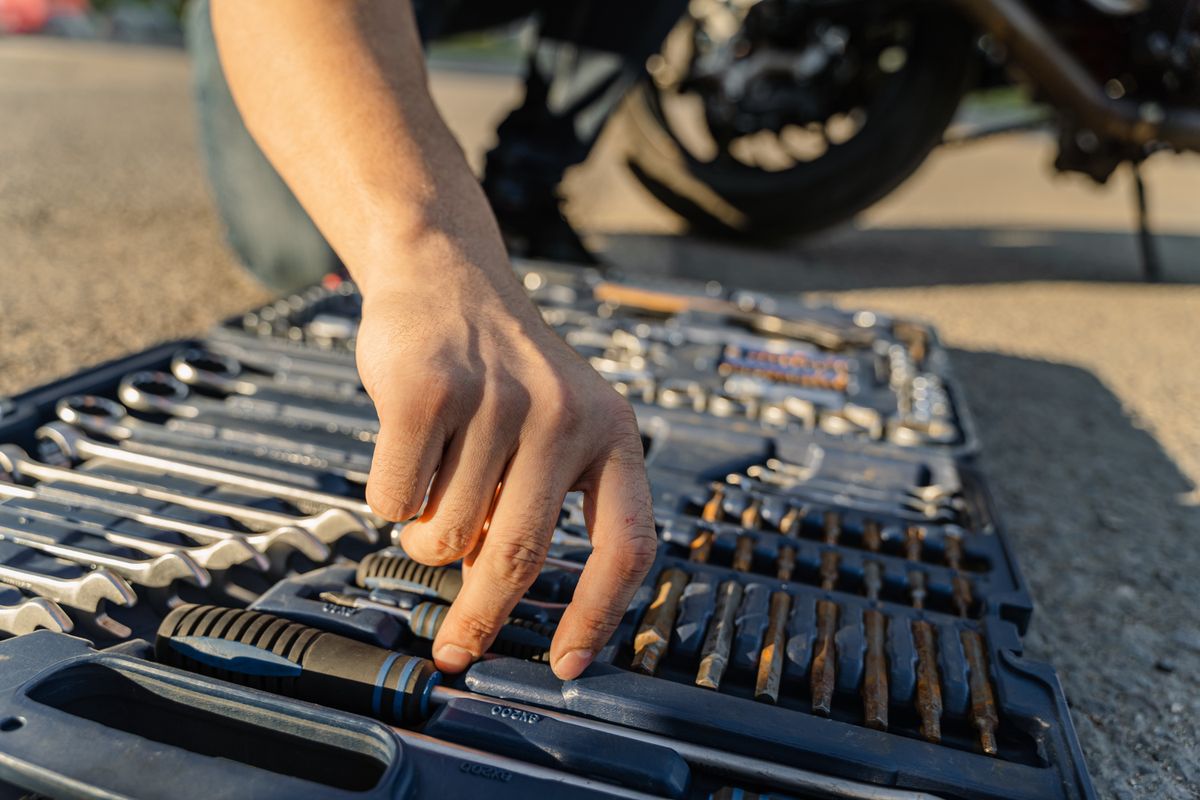 Close-up of a mechanic's hand selecting tools from a toolkit outdoors.