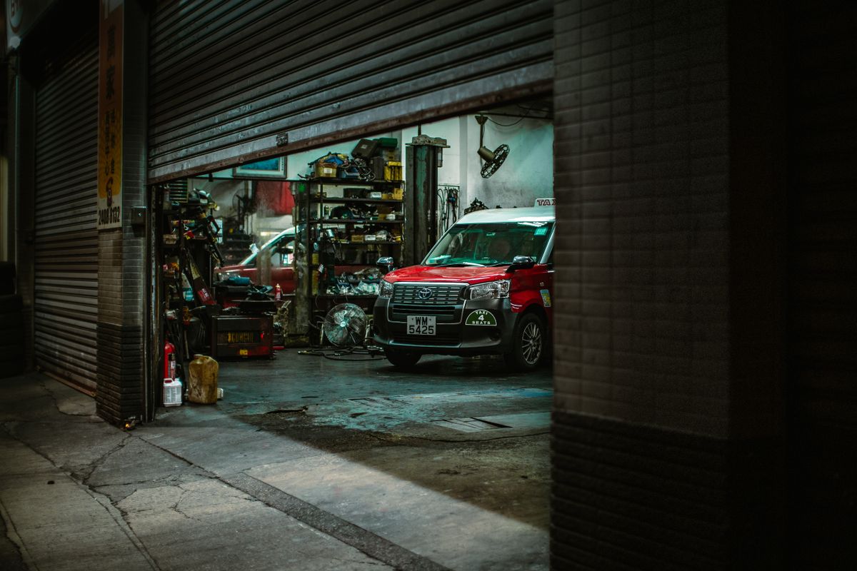 Red car inside a Hong Kong auto repair shop with open roller shutter, showcasing tools and equipment.