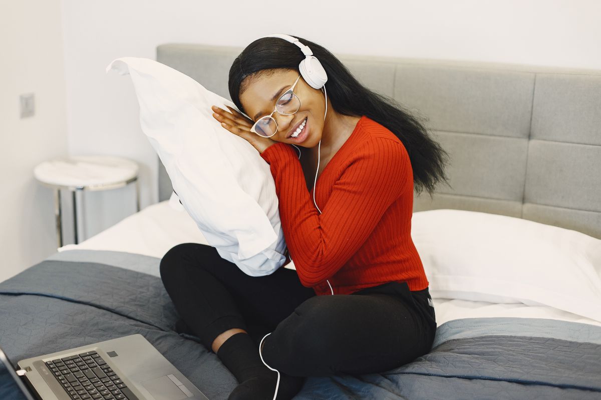 A woman joyfully relaxes with headphones, hugging a pillow in a cozy bedroom.