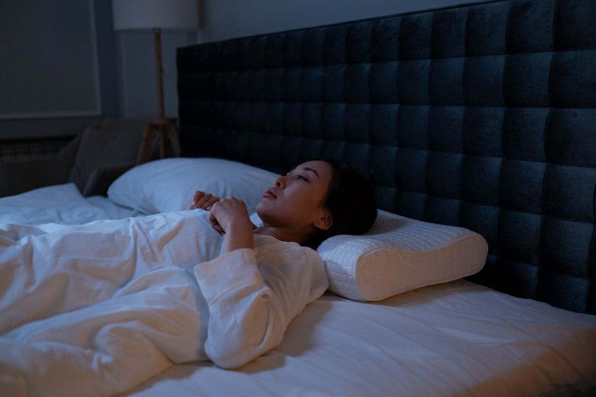 An Asian woman lying awake in bed at night, showing signs of insomnia and sleeplessness.