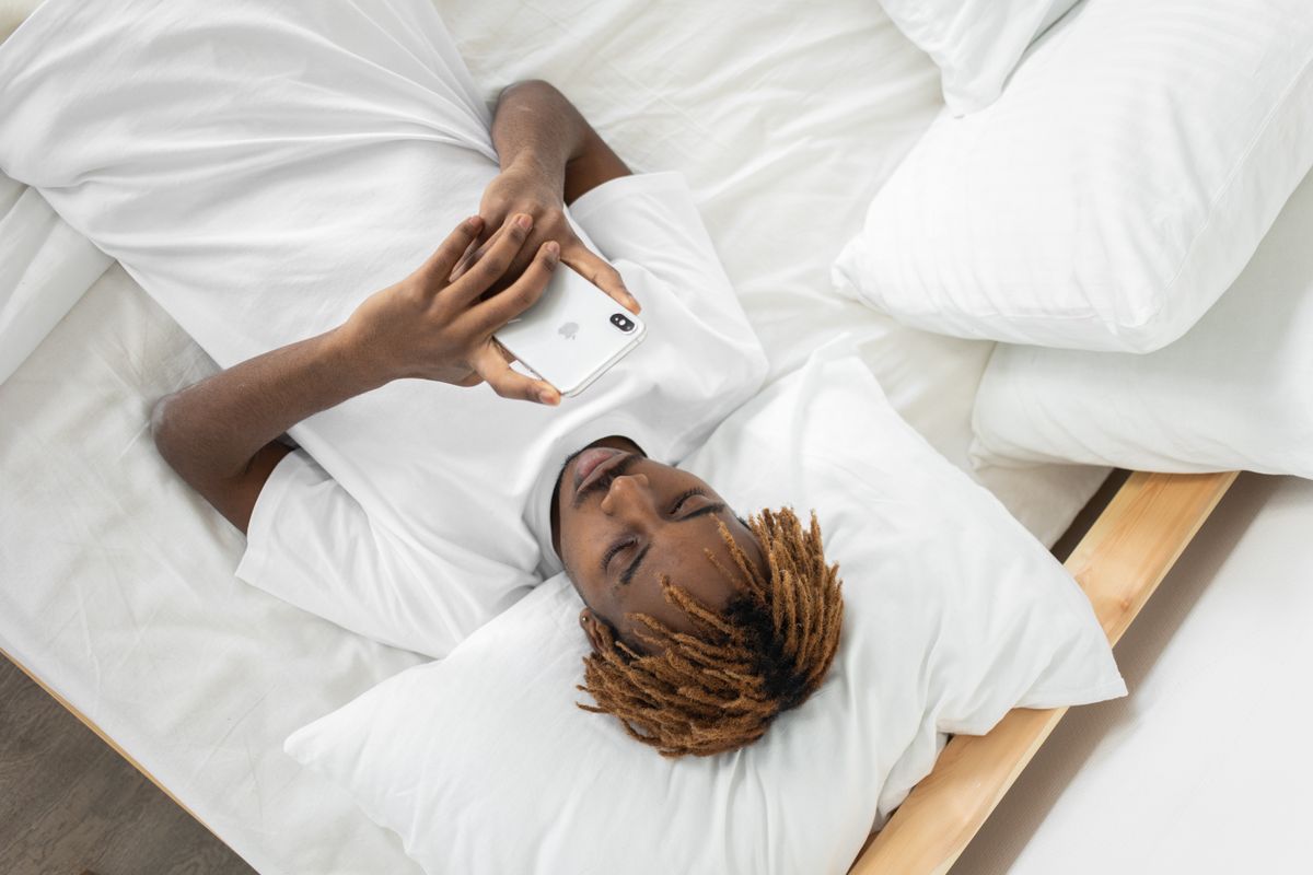Young man lying in bed texting on smartphone, relaxed and comfortable setting.