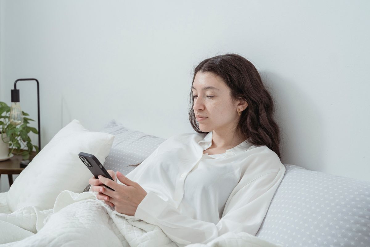 A woman in white long sleeves enjoys a quiet moment in bed, using her smartphone.