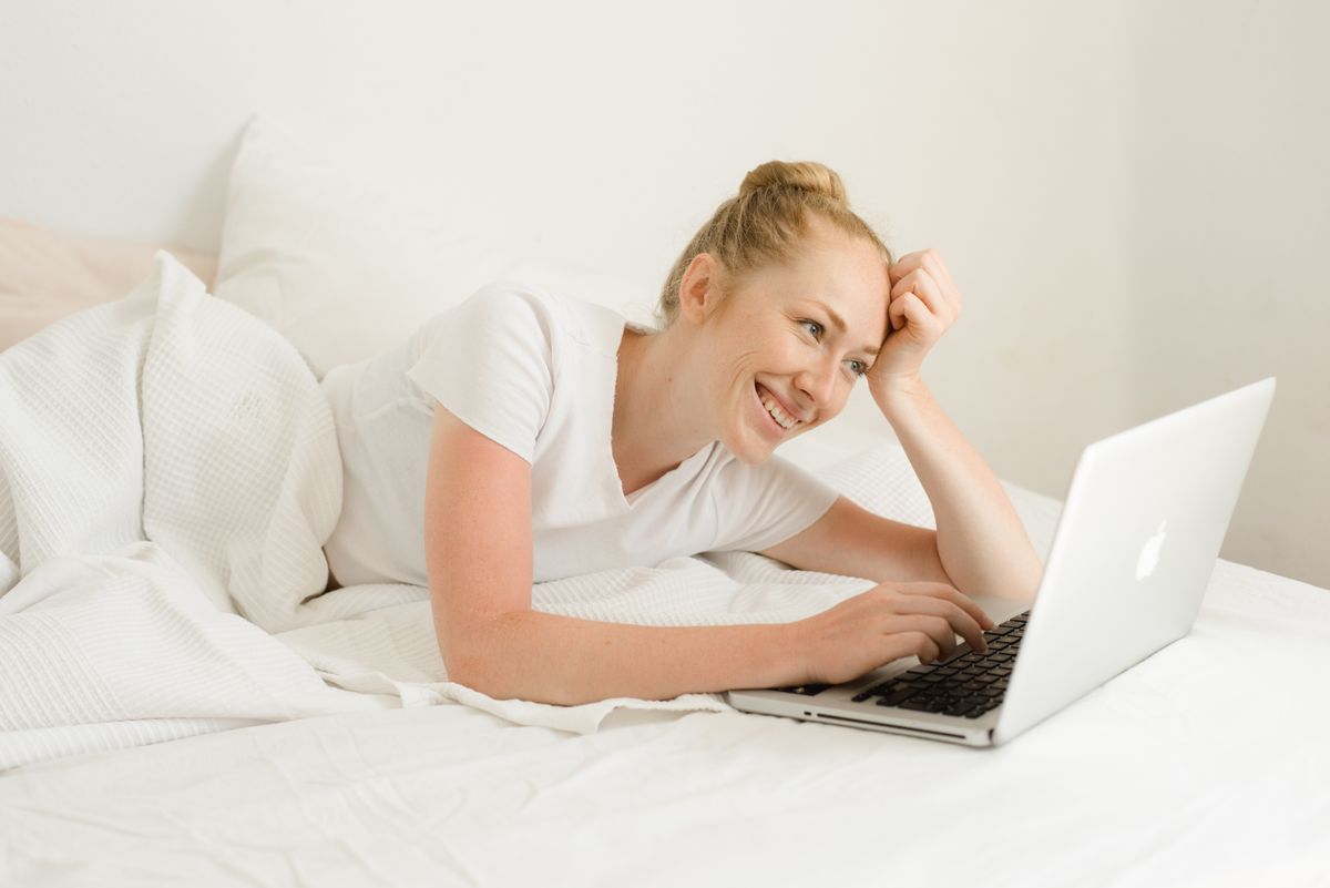 Smiling woman laying on bed using laptop for leisure and relaxation at home.