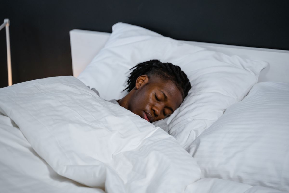 A young man resting peacefully in a bed with white sheets and a dark background.
