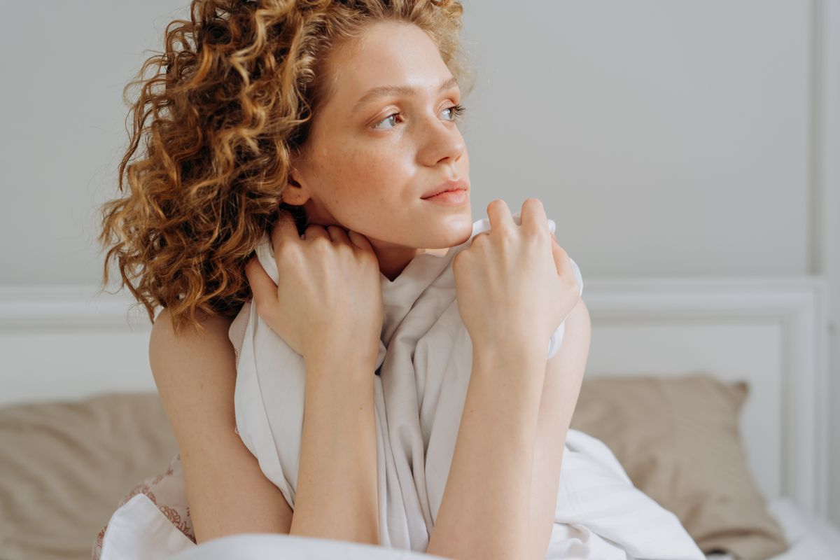 Serene moment of a young woman relaxing in bed, embracing calm and tranquility.