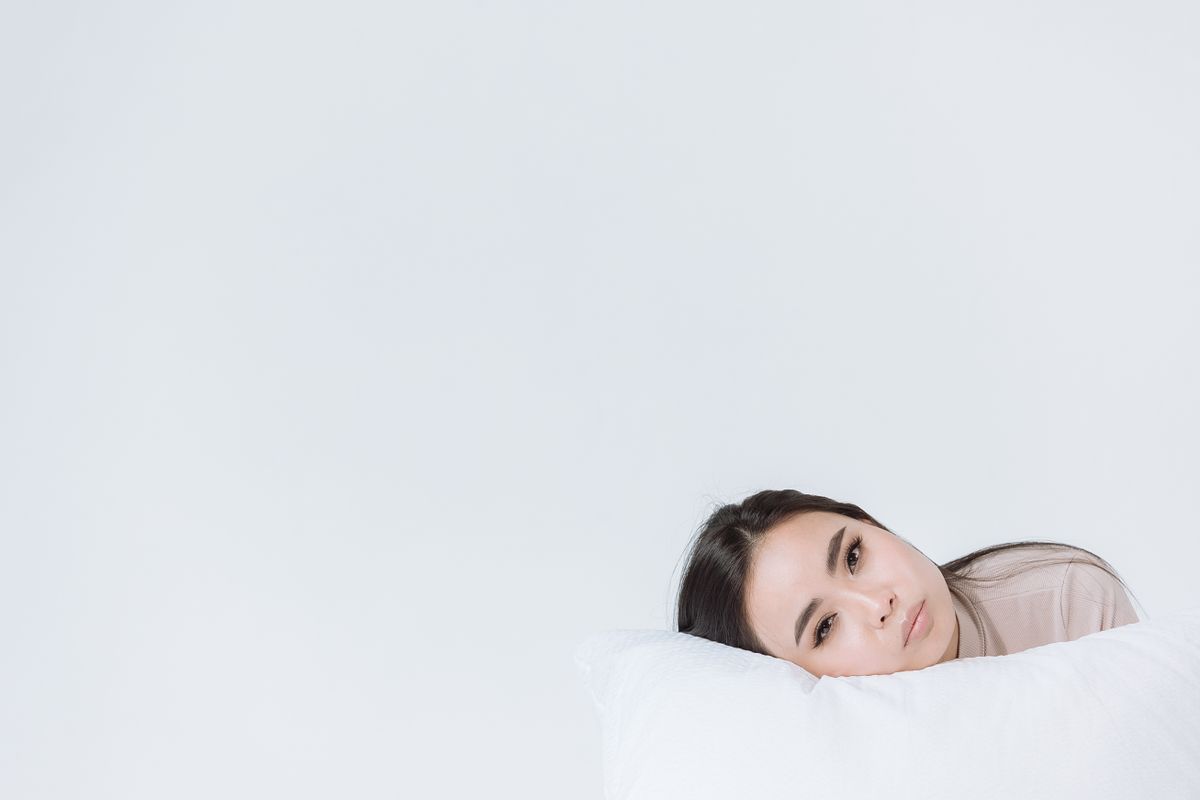 Calm Asian woman resting her head on a white pillow, perfect for beauty and relaxation themes.
