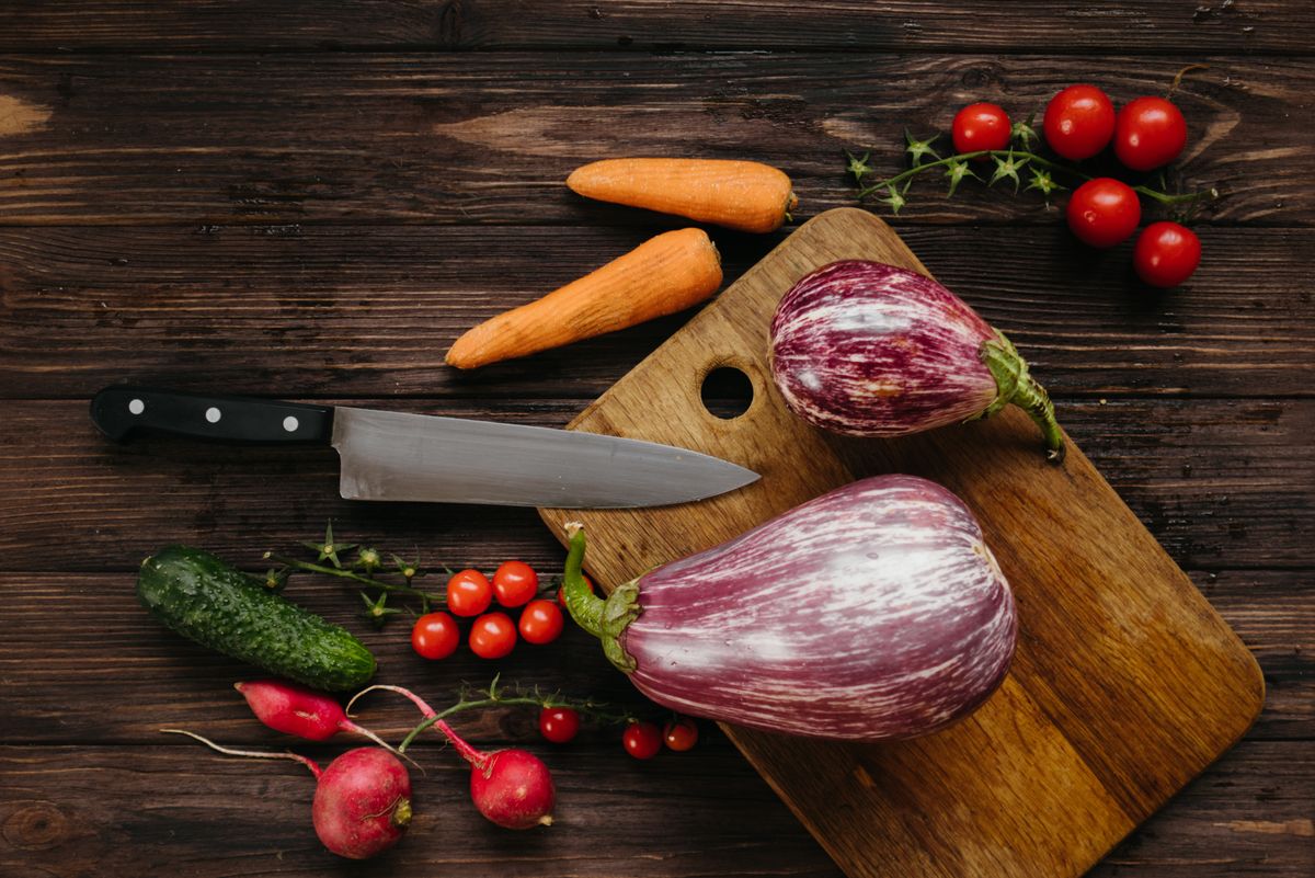 A selection of fresh vegetables with a knife on a wooden board, perfect for healthy cooking concepts.
