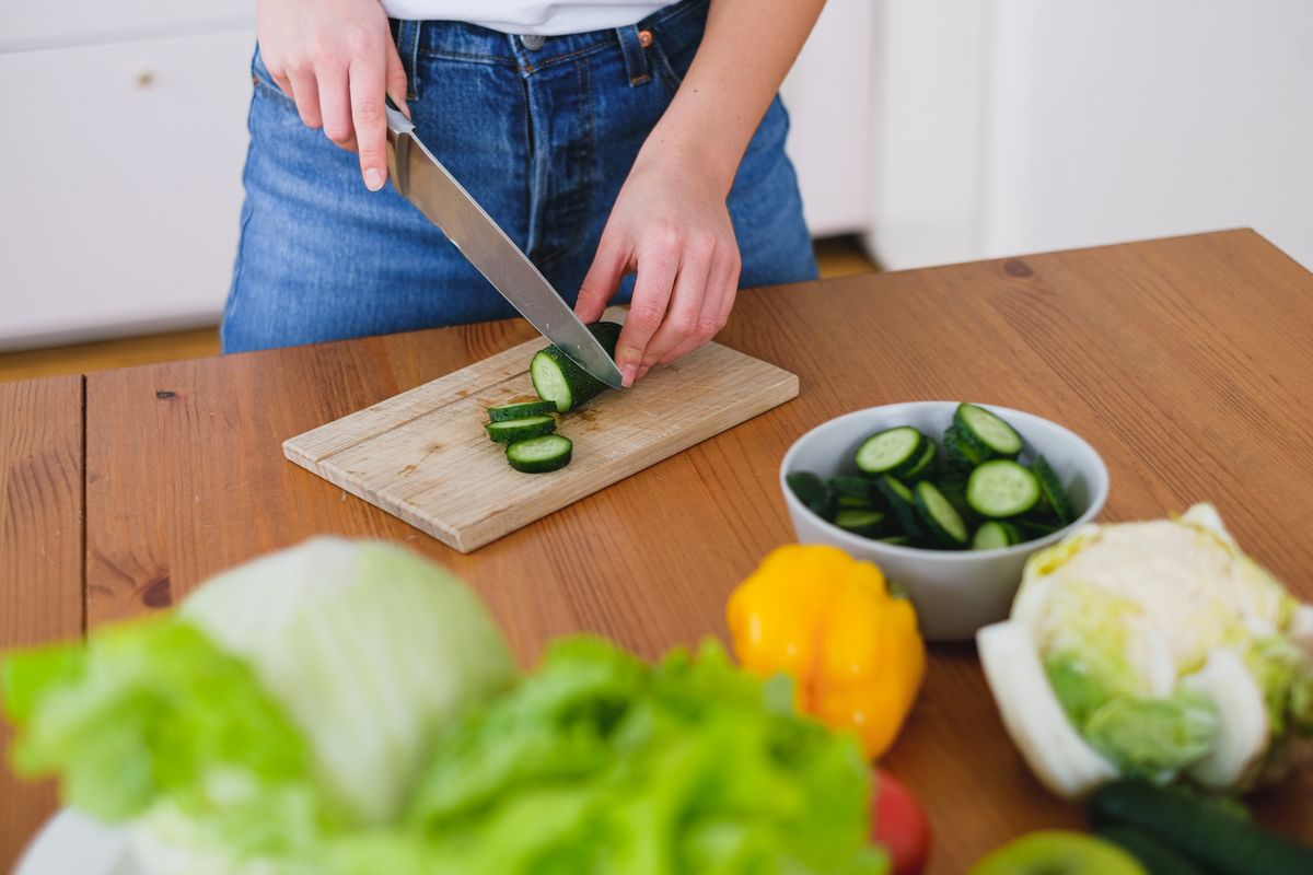 Healthy food preparation with fresh cucumbers and vegetables on a wooden table.