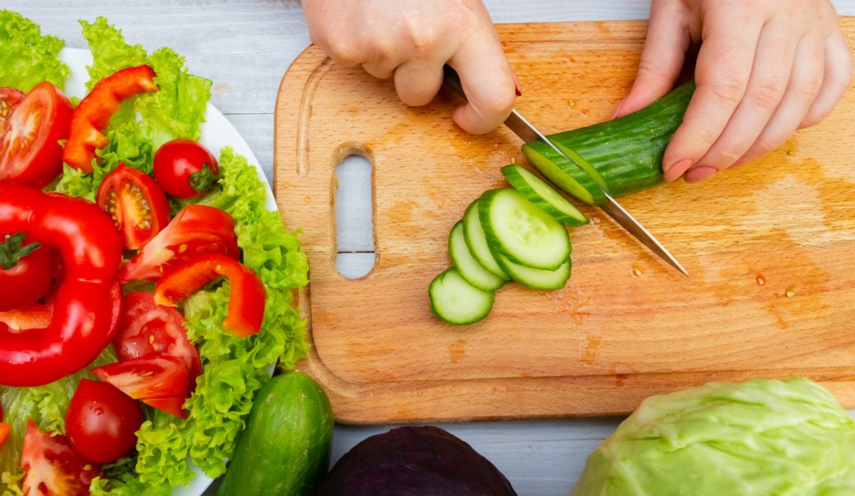 Fresh vegetables being sliced on a cutting board for a healthy meal prep.