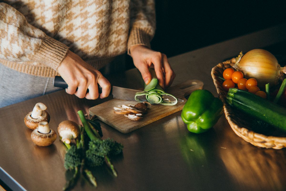 Close-up of hands slicing fresh vegetables on a wooden board in the kitchen.