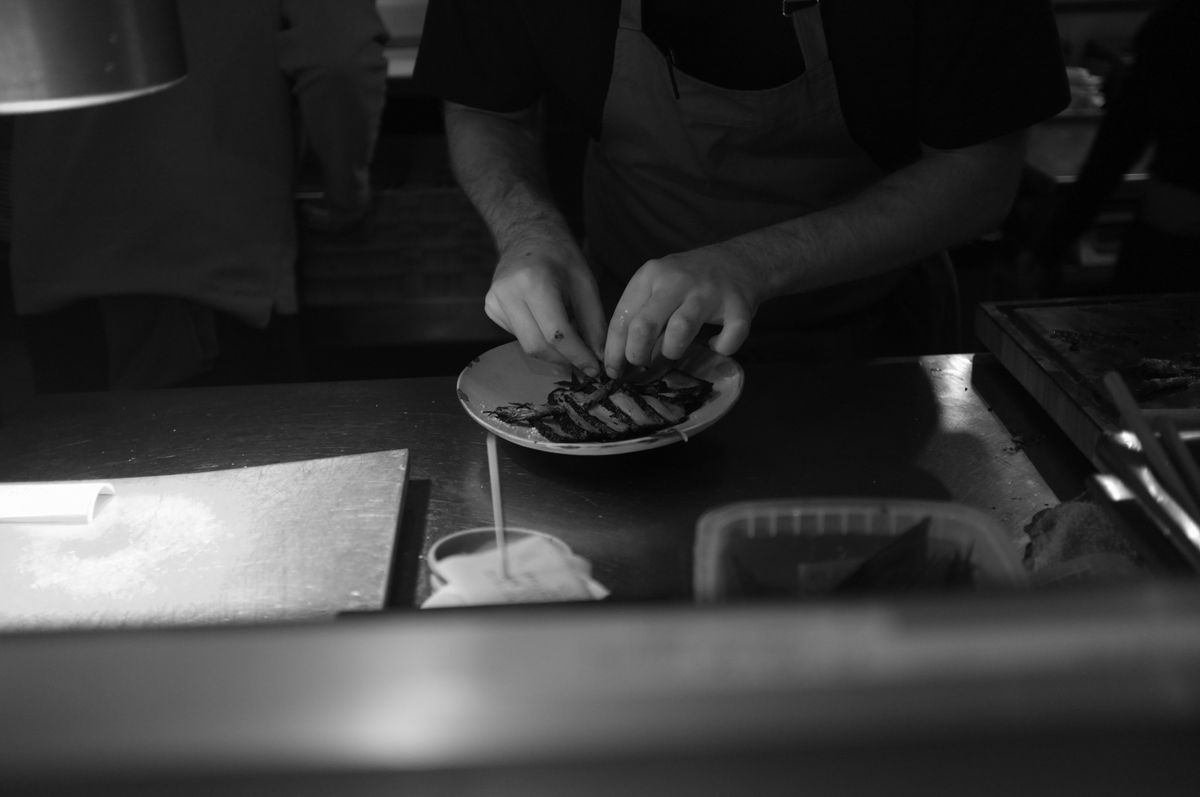 A chef is preparing food in a dimly lit kitchen, focused on presentation.