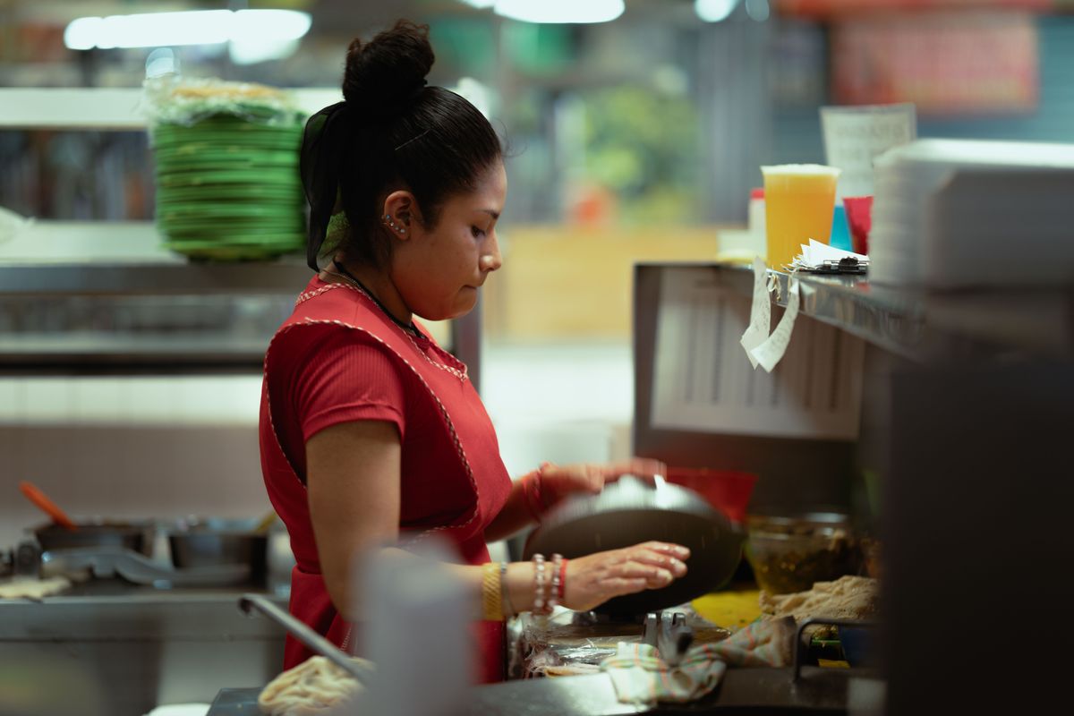 A woman preparing food in a busy Mexico City kitchen, focusing on traditional cooking.