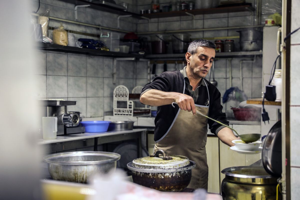 Chef in an apron serving soup in a rustic kitchen setting, creating an authentic dining experience.