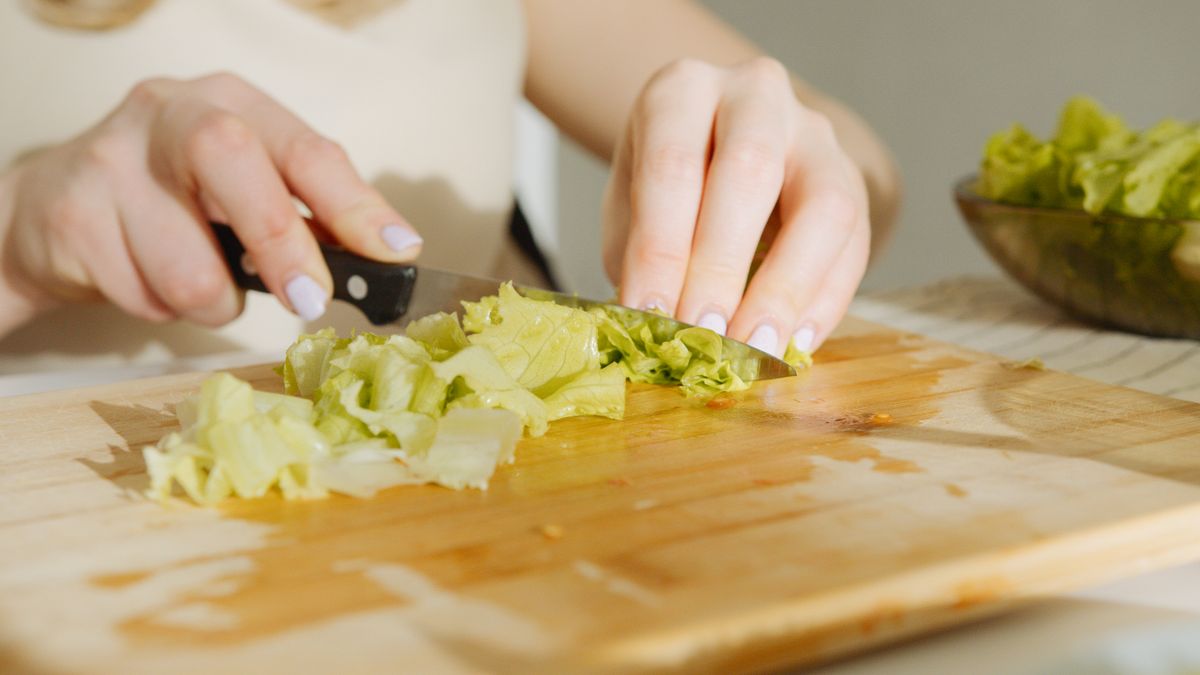 A person slices fresh lettuce on a wooden cutting board, showcasing food preparation techniques.