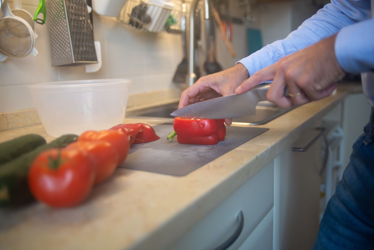 A man slices red bell peppers and tomatoes on a kitchen counter with a knife.