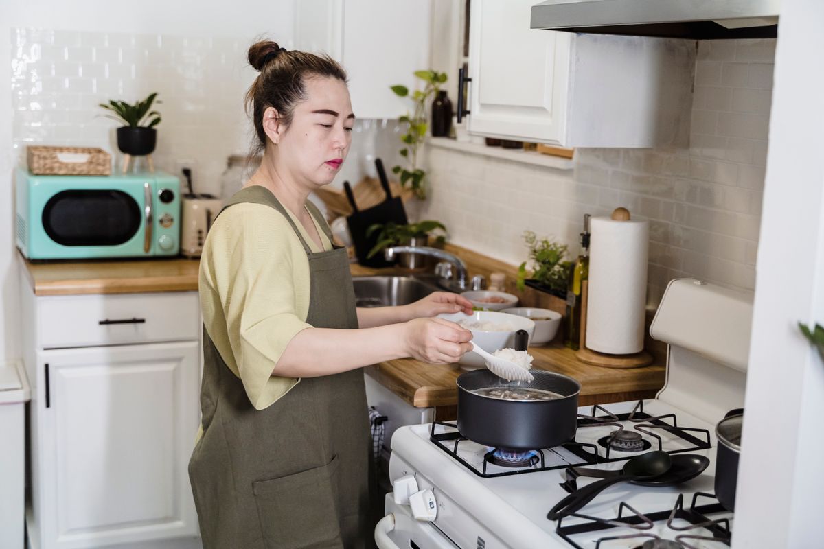 Asian woman preparing a meal in a cozy kitchen with modern appliances.